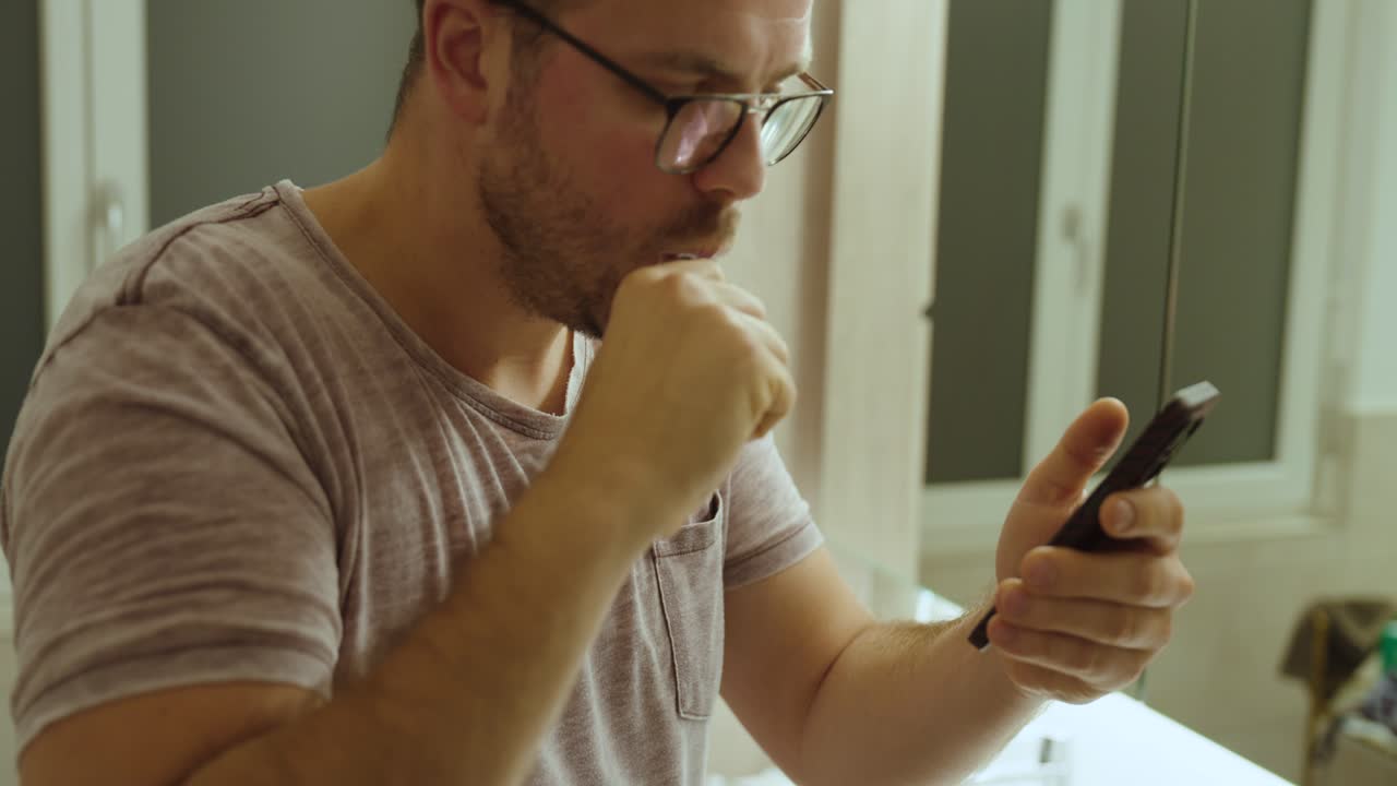 Un uomo si lava i denti mentre guarda il telefono, a simboleggiare la dipendenza dai social media e l'uso costante dello smartphone nella routine quotidiana