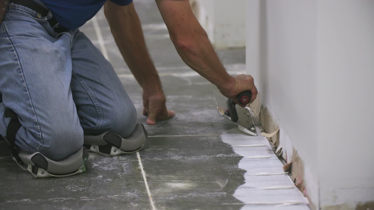 Slow motion footage of a man spreading floor adhesive against a ripped up wall along the floor
