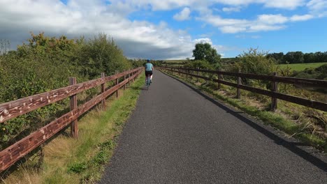 POV-follows-Caucasian-woman-riding-bicycle-on-rural-green-bike-path