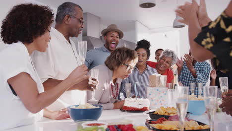 senior black woman blowing out the candle on birthday cake during a celebration with her family