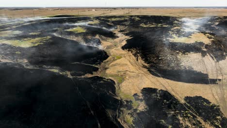 smoke blowing in the wind off freshly burnt prairie after controlled burn in the flint hills of kansas, reverse drone shot