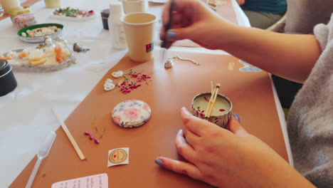 woman placing the decoration with tweezers on the candle during candle creation workshop