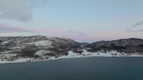 tiro de drone volando sobre el agua hacia una montaña cubierta de nieve en noruega