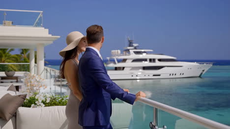 elegant couple overlooking ocean and yacht from luxury resort balcony