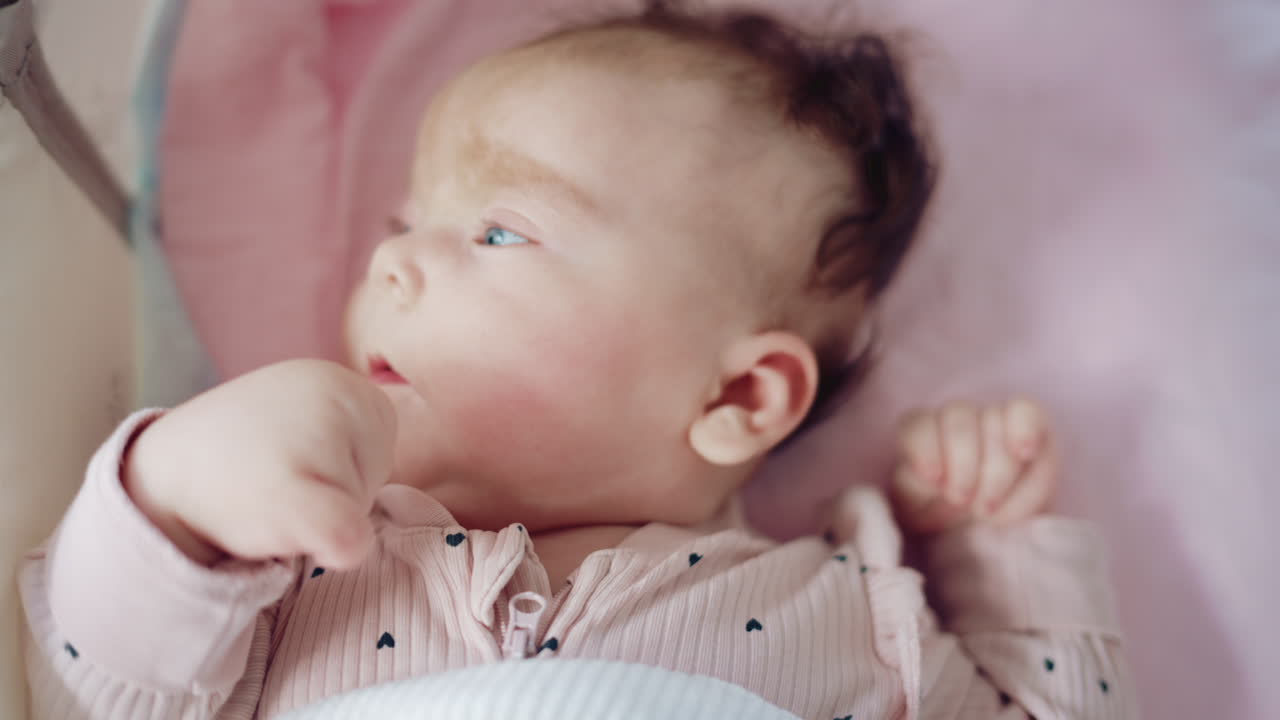 Close up of a baby lying on a soft blanket, wearing a pastel pink outfit