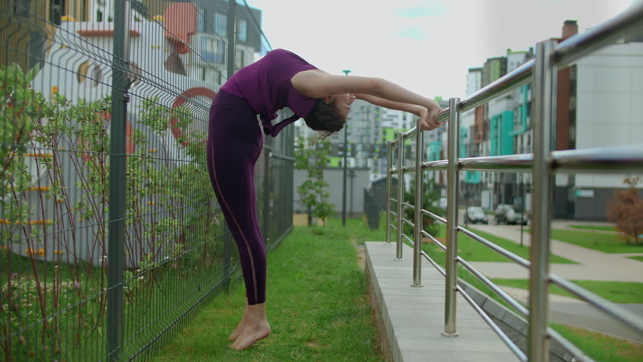 Woman practicing yoga outdoors near metal fence