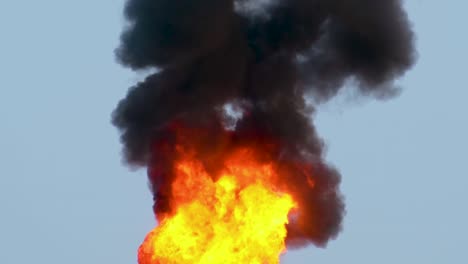 Petroleum-refinery-gas-flare-blazing-fire-pouring-thick-black-smoke-into-the-blue-sky-from-chimney-stack---4K-footage
