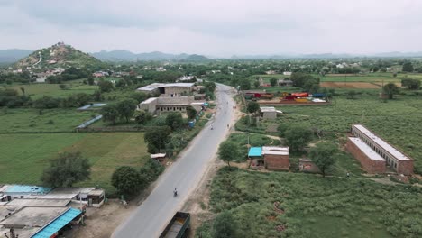 a serene drone panning shot above a lush green indian village, showcasing the vibrant landscape and peaceful rural life. the footage captures rolling fields, traditional houses.