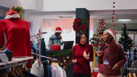 friendly retail assistant in festive ornate shopping mall fashion shop showing client beautiful red garments, ready to be worn at xmas themed holiday events during winter season