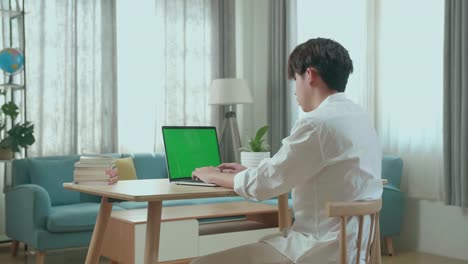 side view of asian man student typing on green screen computer at home