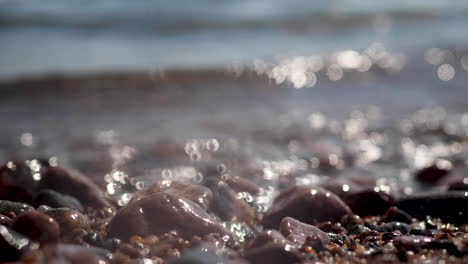 Agua-Que-Se-Lava-Sobre-Guijarros-En-La-Playa-Soleada,-Primer-Plano