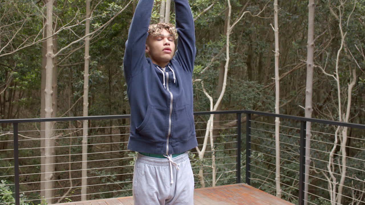 Young man stretching on outdoor deck surrounded by trees, enjoying nature