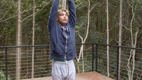 young man stretching on outdoor deck surrounded by trees, enjoying nature