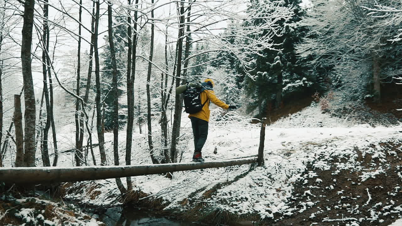 Caminhante atravessando um riacho em uma floresta de inverno com neve