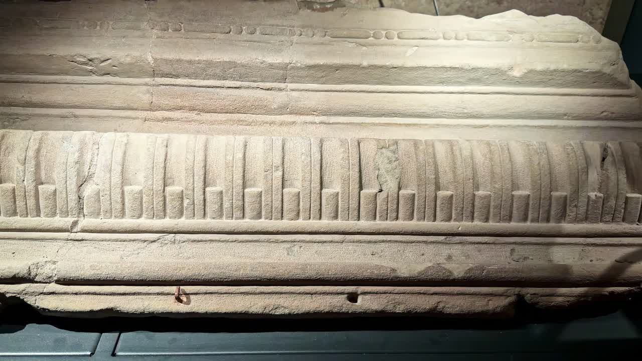Primo piano di fregio in pietra calcarea scolpita e modanatura del cornicione in un'esposizione museale, che mostra elementi decorativi medievali in pietra, segni di scalpello e dettagli della superficie alterata dagli agenti atmosferici