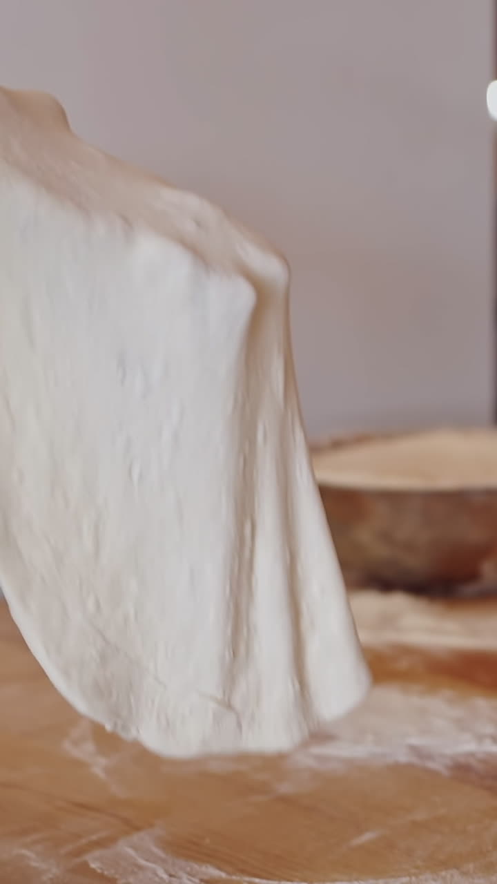 Male hands prepares dough for pizza. Baker making pizza dough on wooden table before baking. Cook forming the dough with his hands on a round deco. Close-up. Vertical video