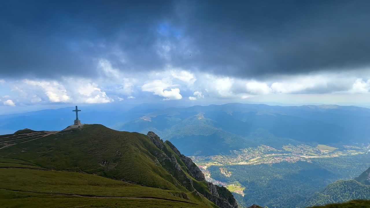 Un paesaggio nuvoloso cupo e drammatico copre il cielo sopra i Carpazi meridionali. Vista sul monumento Cross Memorial sulla vetta verde Caraiman nei monti Bucegi, Romania