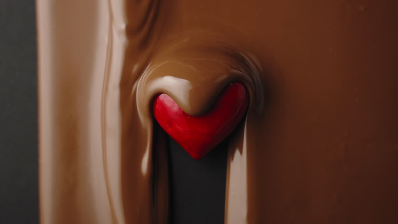 el chocolate con leche fluye sobre el corazón rojo en cámara lenta
