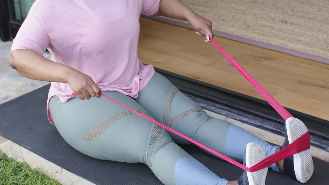 Donna posiziona una fascia rossa intorno alle scarpe sul patio, tirando le maniglie verso la vita per tonificare il busto