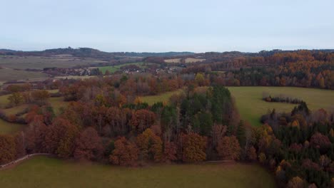 flying above autumnal rural landscape with fields, forests and a village