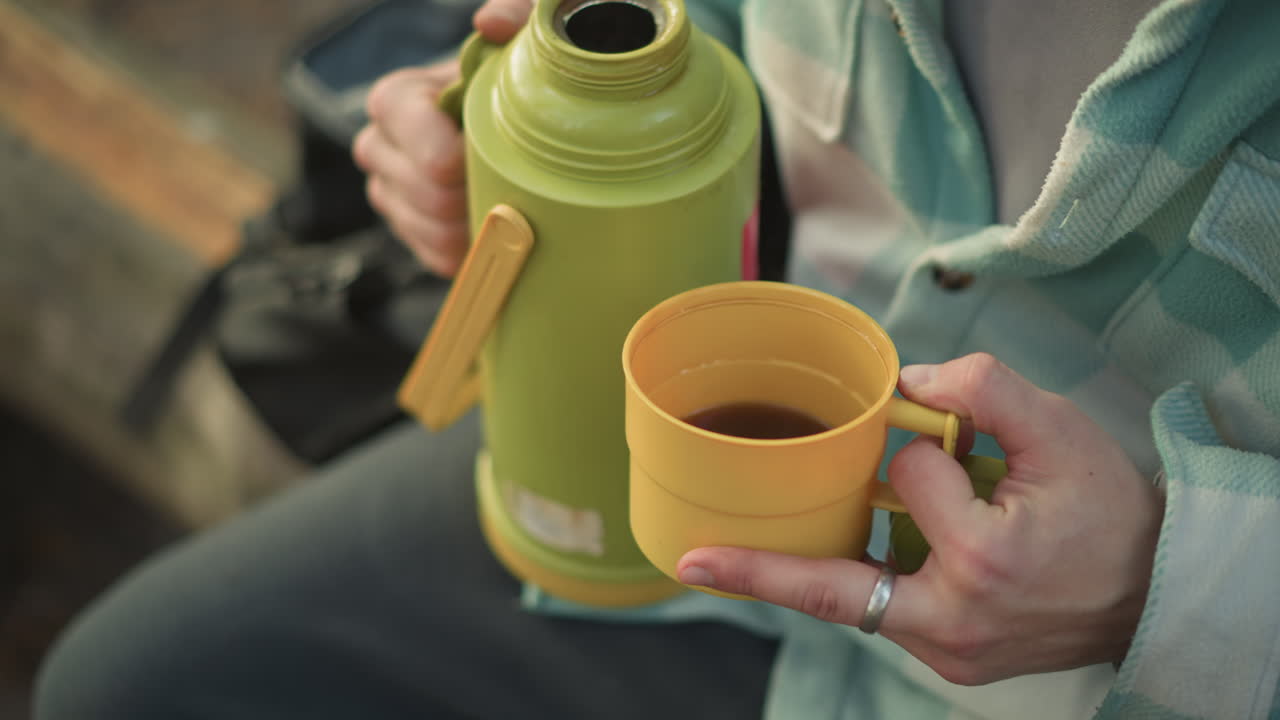 Escursionista che prepara il caffè all'aperto, escursionista che versa una bevanda durante una pausa, foto panoramica all'aperto di un viaggiatore con bevanda calda ed equipaggiamento, escursionista su sentiero si ferma per gustare un caffè con l'attrezzatura su una panchina