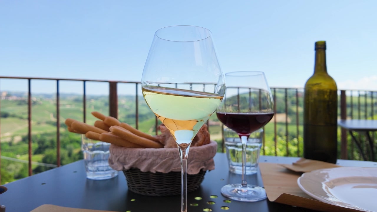 Vino bianco che volteggia in un bicchiere su un tavolo all'aperto con vista sui vigneti in Piemonte.