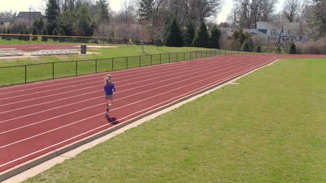 teen girl on a track running by and away from camera on a pretty day