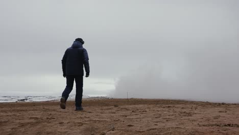 el turista camina por el suelo de grava volcánica naranja hacia la nube de humo blanco.