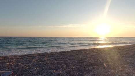 Slow-motion-pan-over-trash-thrown-away-on-beach-at-ocean-during-sunset