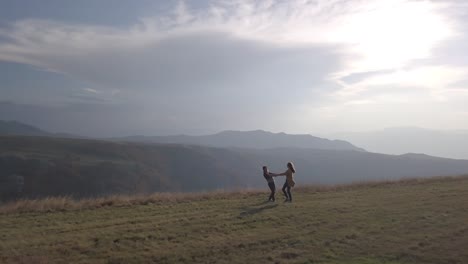 aerial view of romantic couple of young man and woman holding hands and whirling in field, surrounded by picturesque mountain autumn landscape. drone flies around. love story honeymoon. montenegro