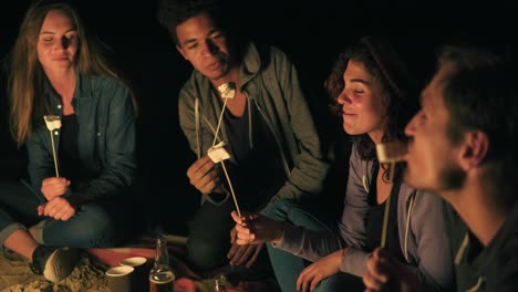 group of happy multiethnic friends camping by the fire at night laughing and roasting marshmallows