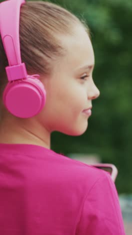 a young girl in a bright pink outfit enjoys music on her smartphone with matching headphones, capturing a joyful moment of connection and entertainment