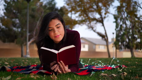 primer plano de una joven hispana leyendo las páginas de un libro de cuentos acostado al aire libre en el parque