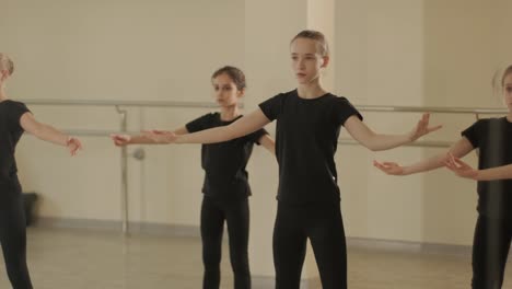 a group of young ballet students in black dancewear practicing positions in a spacious ballet studio with wooden flooring and wall-mounted barres. focused expressions and synchronized movements.