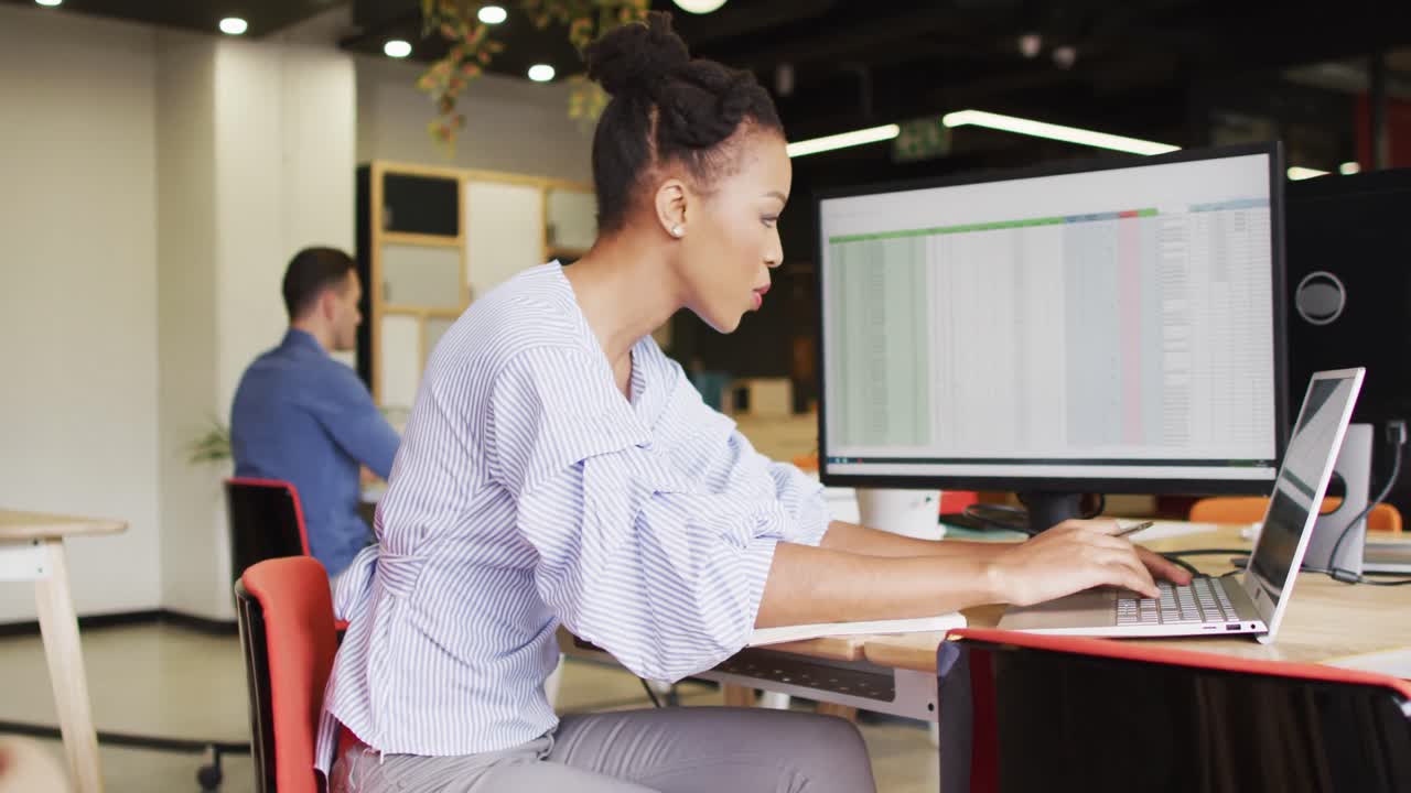 행복 한 아프리카계 미국인 사업가 가 책상 에 앉아 사무실 에서 노트북 을 사용 하고 있다
