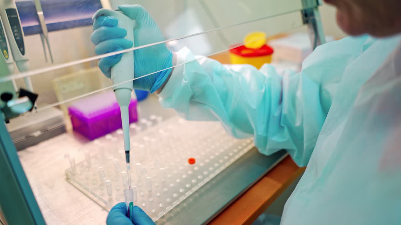 Medical assistant works with test tubes. Researcher in protective uniform dripping liquid into vials with special instrument. Close-up.