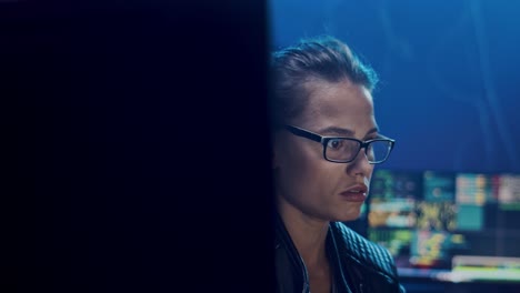 Portrait-Of-The-Young-And-Pretty-Woman-In-Glasses,-Software-Developer-Or-Hacker-Working-At-Night-At-The-Big-Screen-Of-Computer-In-The-Dark-Room-And-Then-Smiling-To-The-Camera-Happily