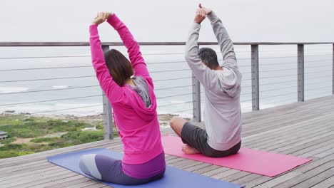 pareja feliz diversa haciendo yoga, sentada y estirándose en el balcón