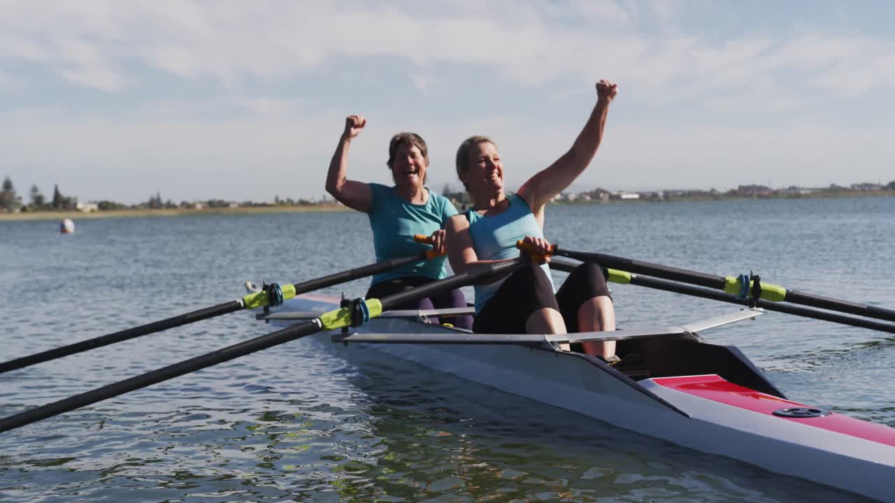 Two senior caucasian women in rowing boat raising hands and cheering