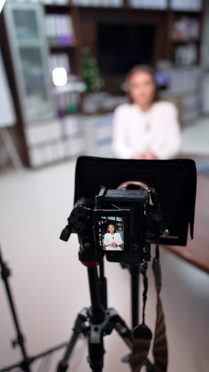 Attractive Caucasian female talks on the display of camera on tripod. Close up. Video content creation for blog. Blurred backdrop. Vertical video.