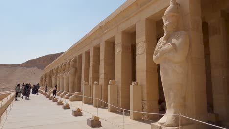 looking across row of colonnade at the mortuary temple of hatshepsut on sunny day with tourists