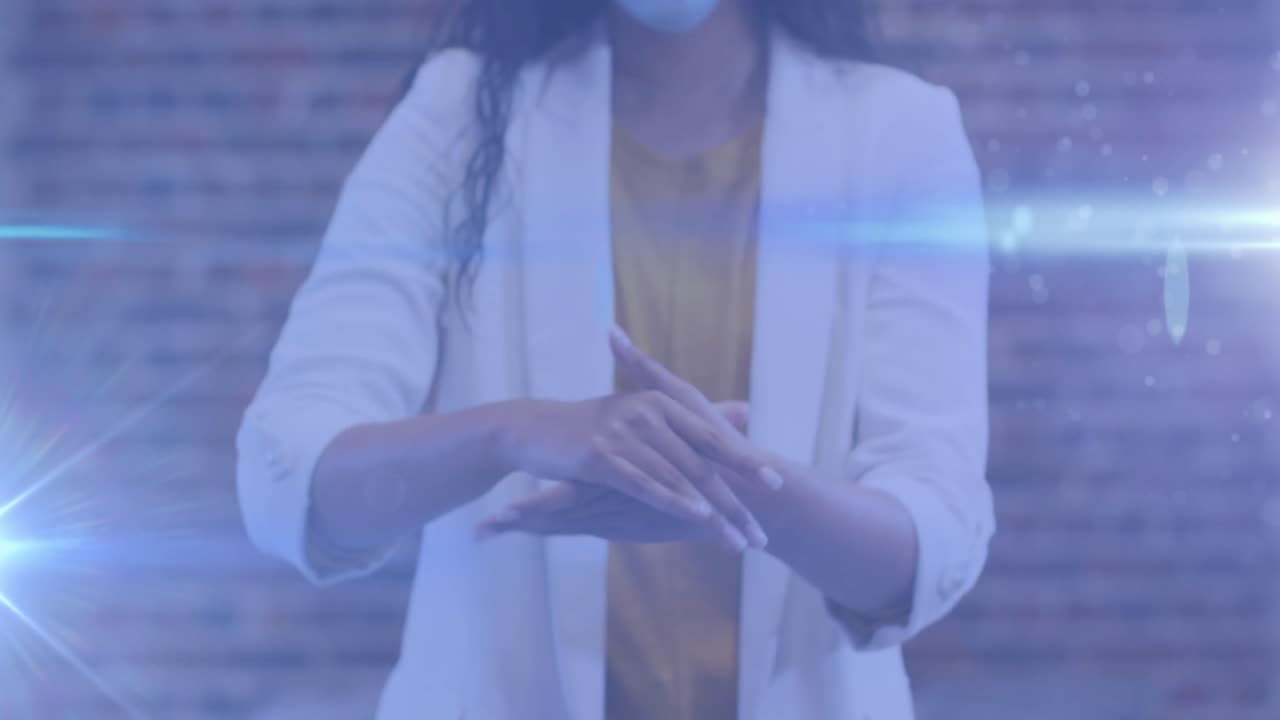 manchas de luz contra la sección media de la mujer con máscara facial usando desinfectante para manos en la oficina