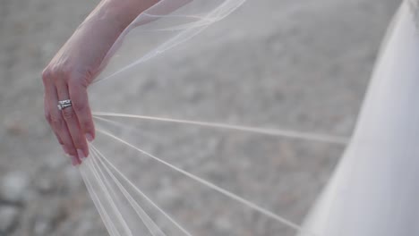 primer plano en cámara lenta de la mano de una novia con un anillo de bodas mostrando mientras sostiene su vil mientras sopla suavemente en el viento.