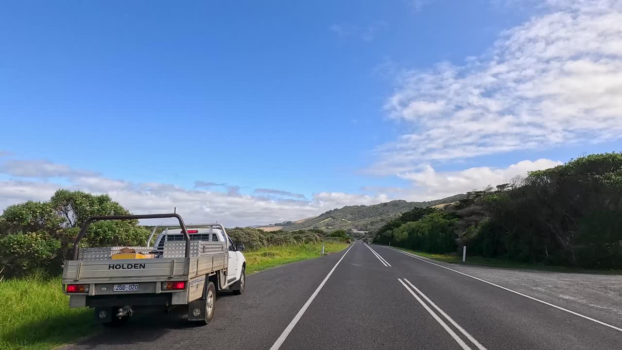 A serene drive on Great Ocean Road with lush greenery, clear skies, and a winding path captured in daylight