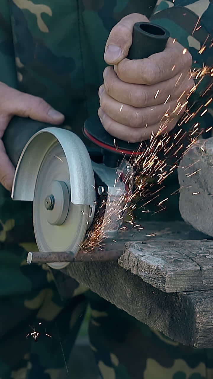 closeup craftsman in camouflage wear cuts metal rod with modern instrument on table in house yard