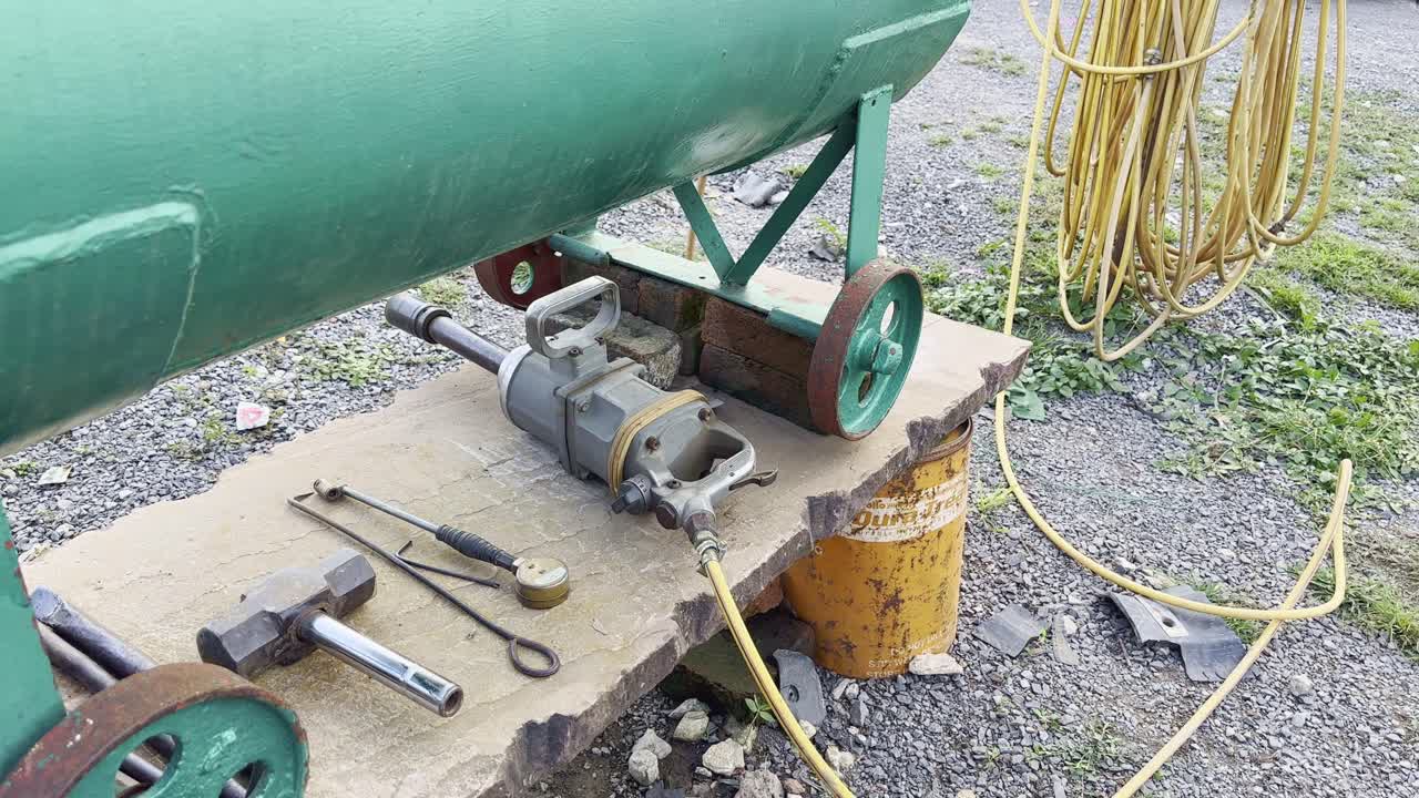 Camera circles around tools and heavy pneumatic wrench connected to an air compressor, used for loosening truck tire bolts at a roadside repair shop in India