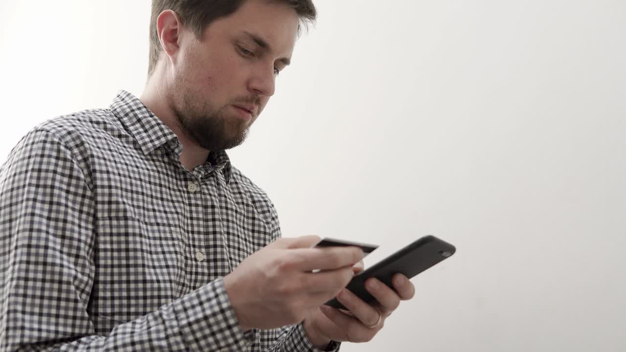 un joven introduce los datos de una tarjeta bancaria en un teléfono inteligente para pagar una compra