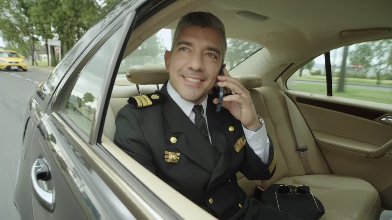 Un pilota effettua una telefonata seduto sul sedile del passeggero di un'auto nera che lo sta portando