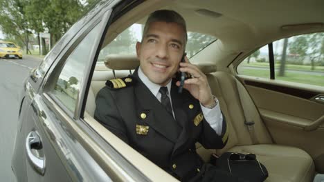 a pilot makes a phone call while sitting in the passenger seat of a black car that drives him