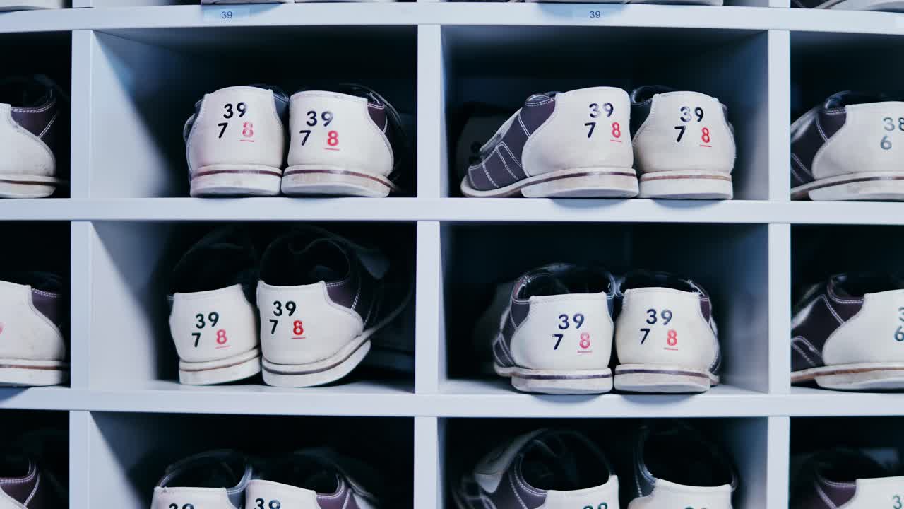 Bowling rental shoes with visible size tags lined up inside white storage rack